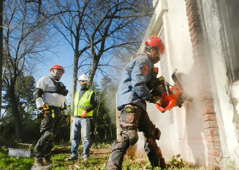 Cuadrilla de albañiles demoliendo fachada de edificio antiguo con equipos de protección en Huelva